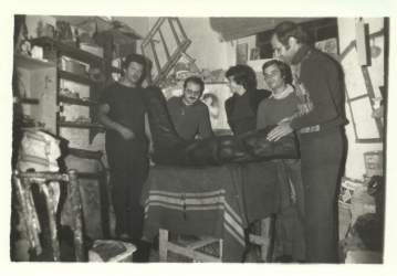 Fotografia in bianco e nero: un gruppo di persone in uno studio d’artista attorno a un tavolo