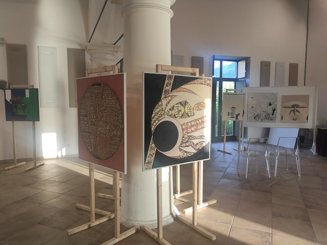 Opere esposte su cavalletti accanto alle colonne della sala